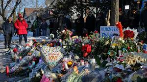Flowers, signs, and other memorial items arranged along a snowy roadside.