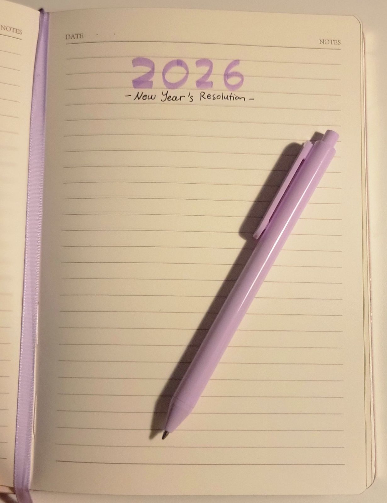 Open notebook page labeled “2026 — New Year's Resolution” with two pink pens resting on it.