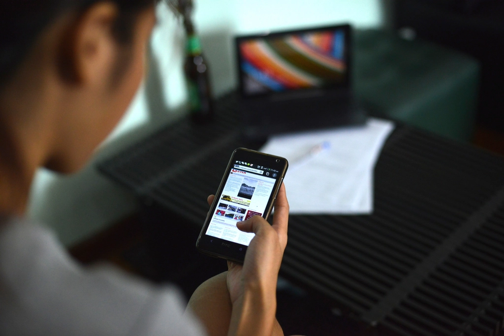 Person holding and looking at a smartphone near a laptop