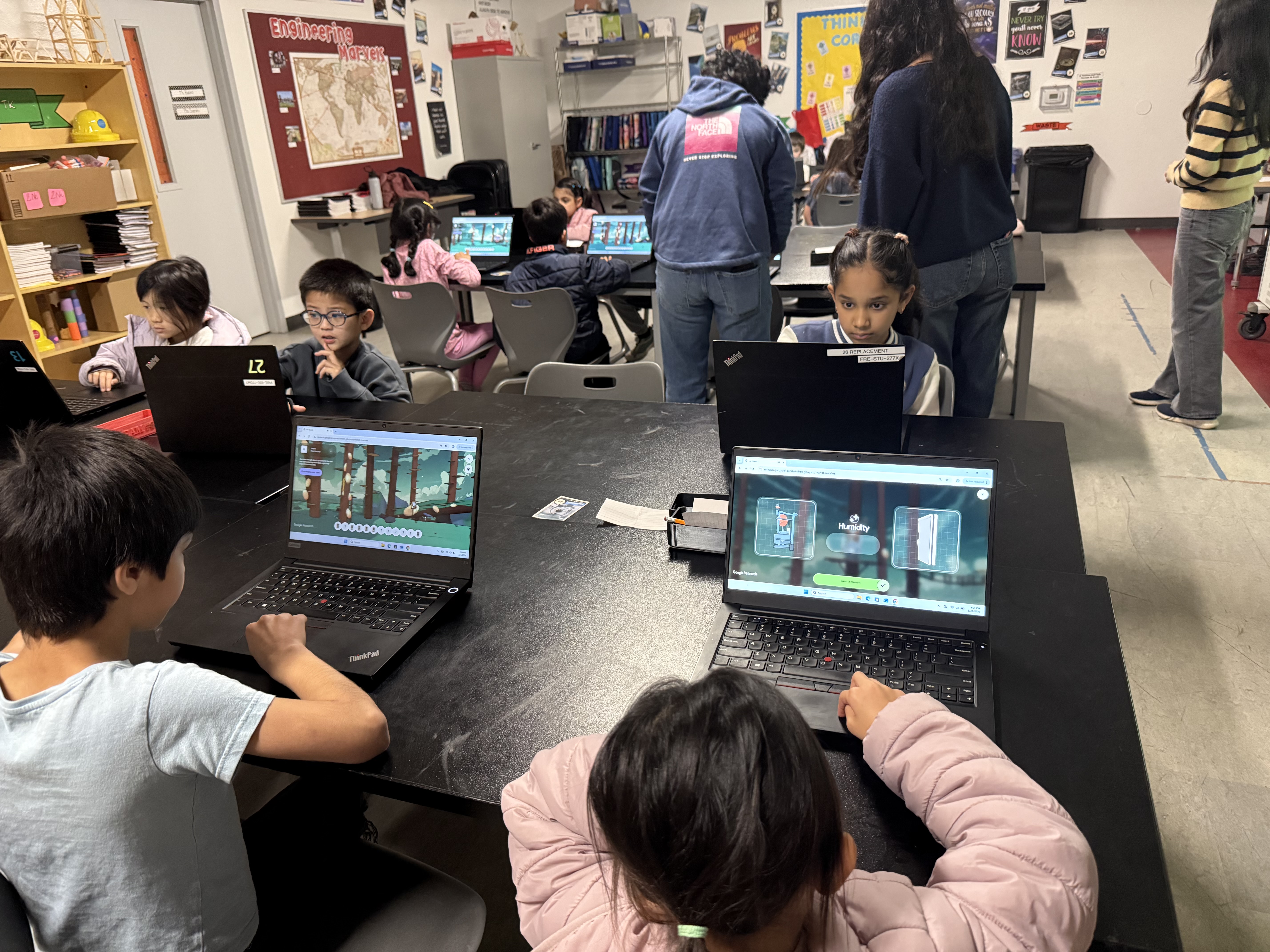 Students work together at tables on laptops in a classroom.