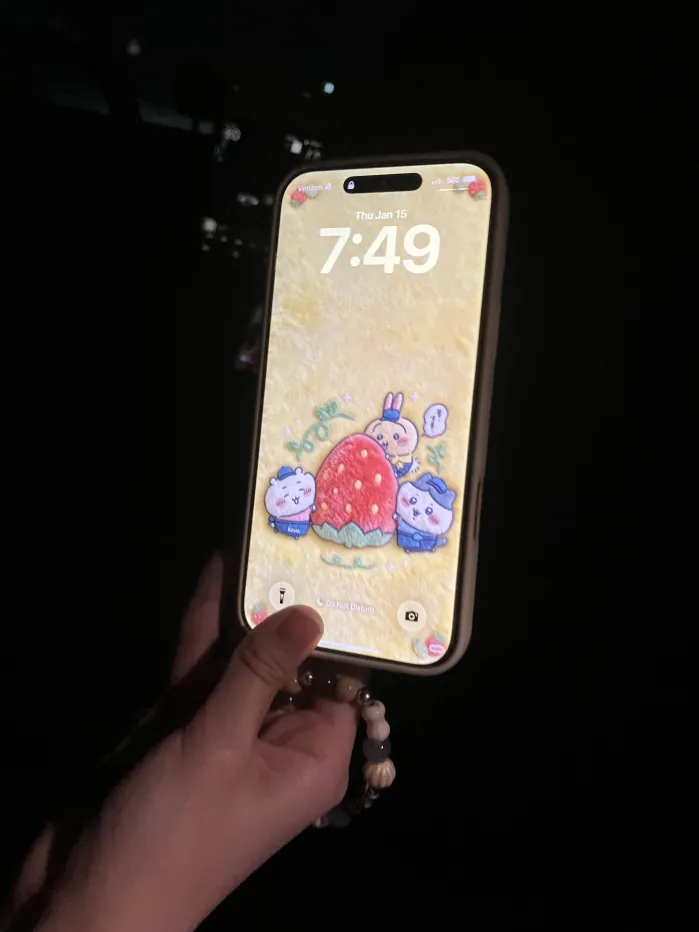 Front of a smartphone showing a lock screen with a colorful character wallpaper, held in a hand