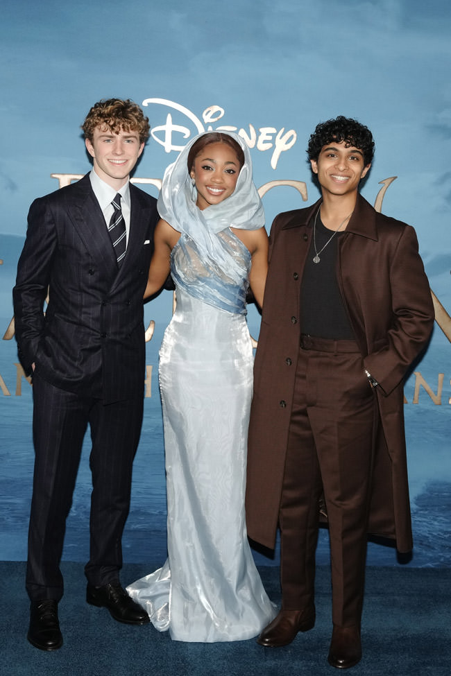 Three people in formal clothing pose together on a Disney-branded event backdrop.