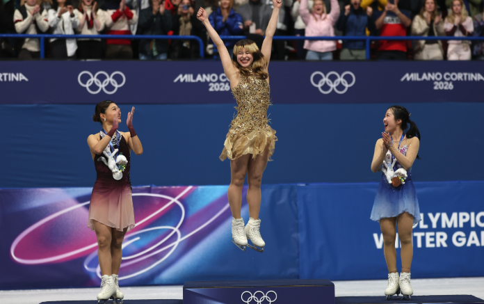 Figure skater in a gold costume stands on a podium with two other skaters.