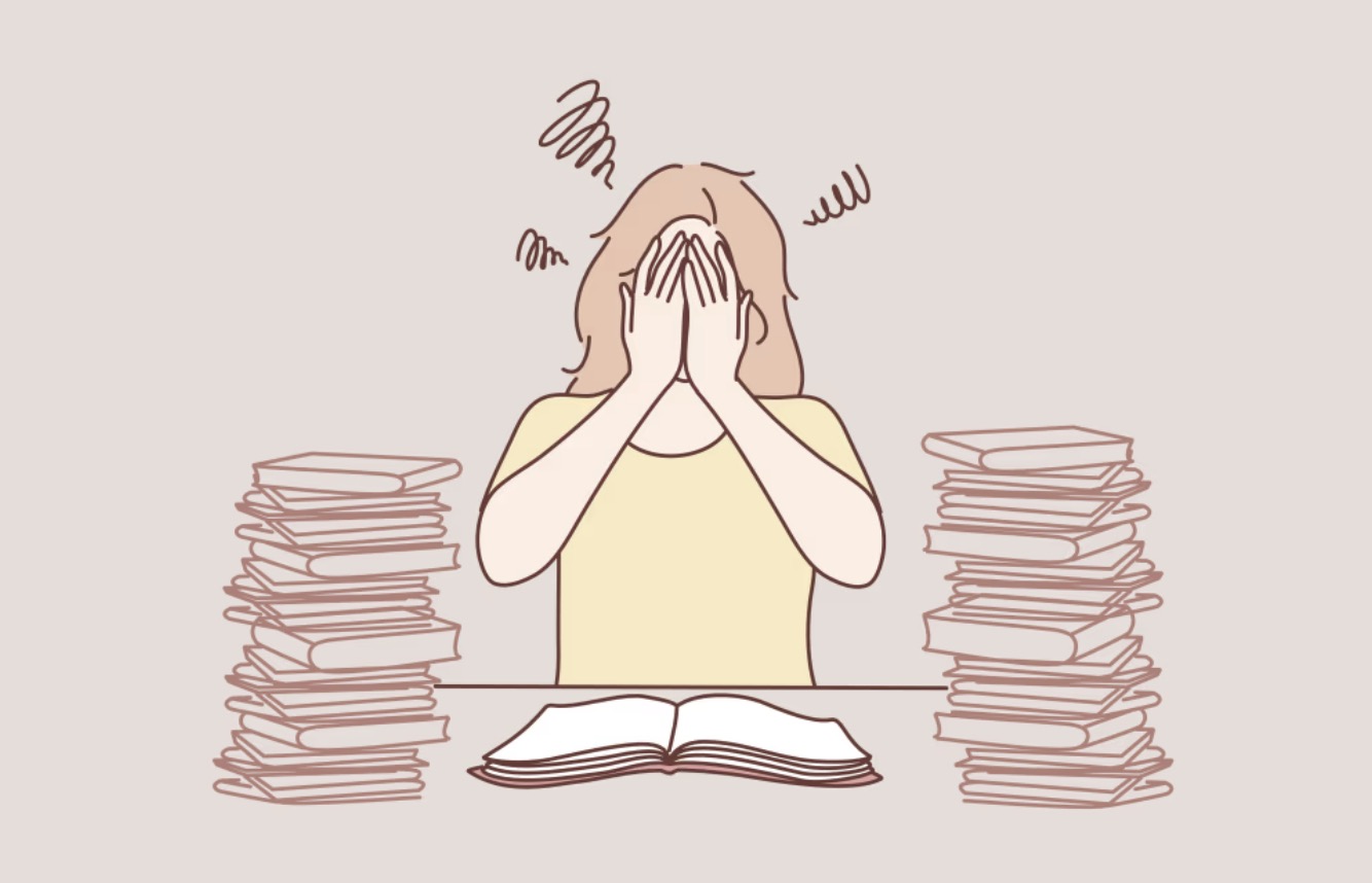 Illustration of a student covering their face at a desk between stacks of books, with an open book in front of them.