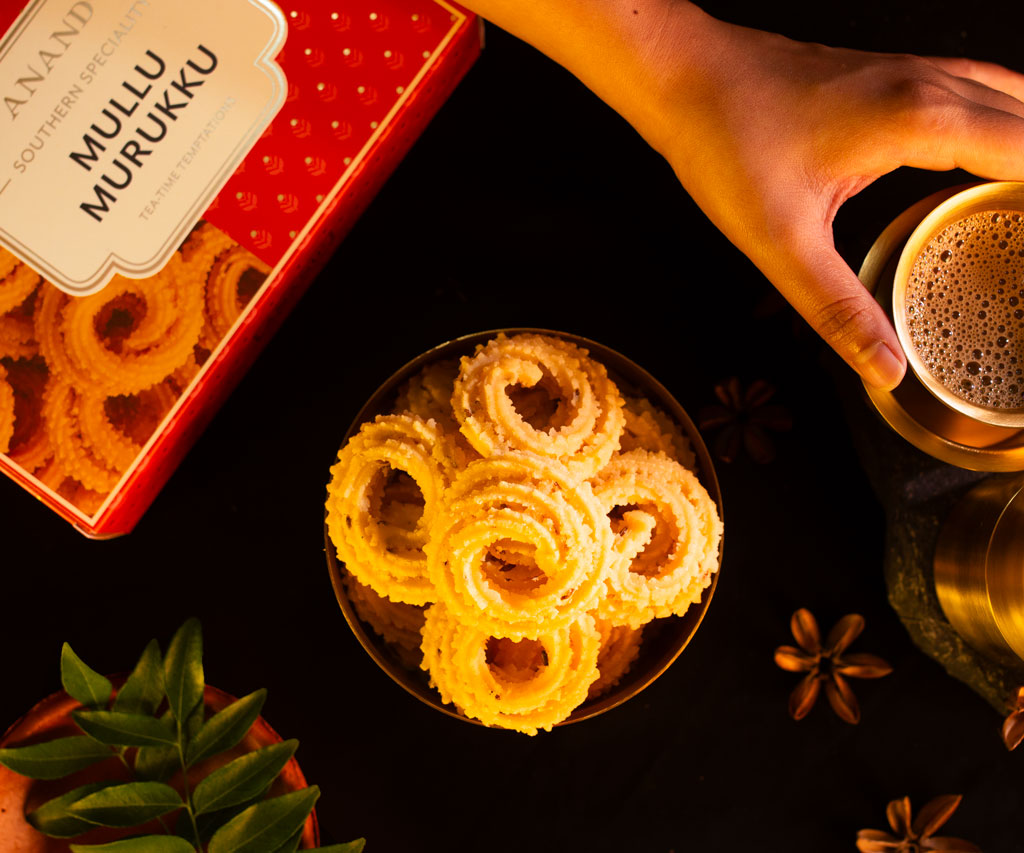 Flatlay shot of Anand Sweet's mullu murukku placed inside a tiffin box, a hand comes and picks up one of the murukku, indian south Indian snack photography