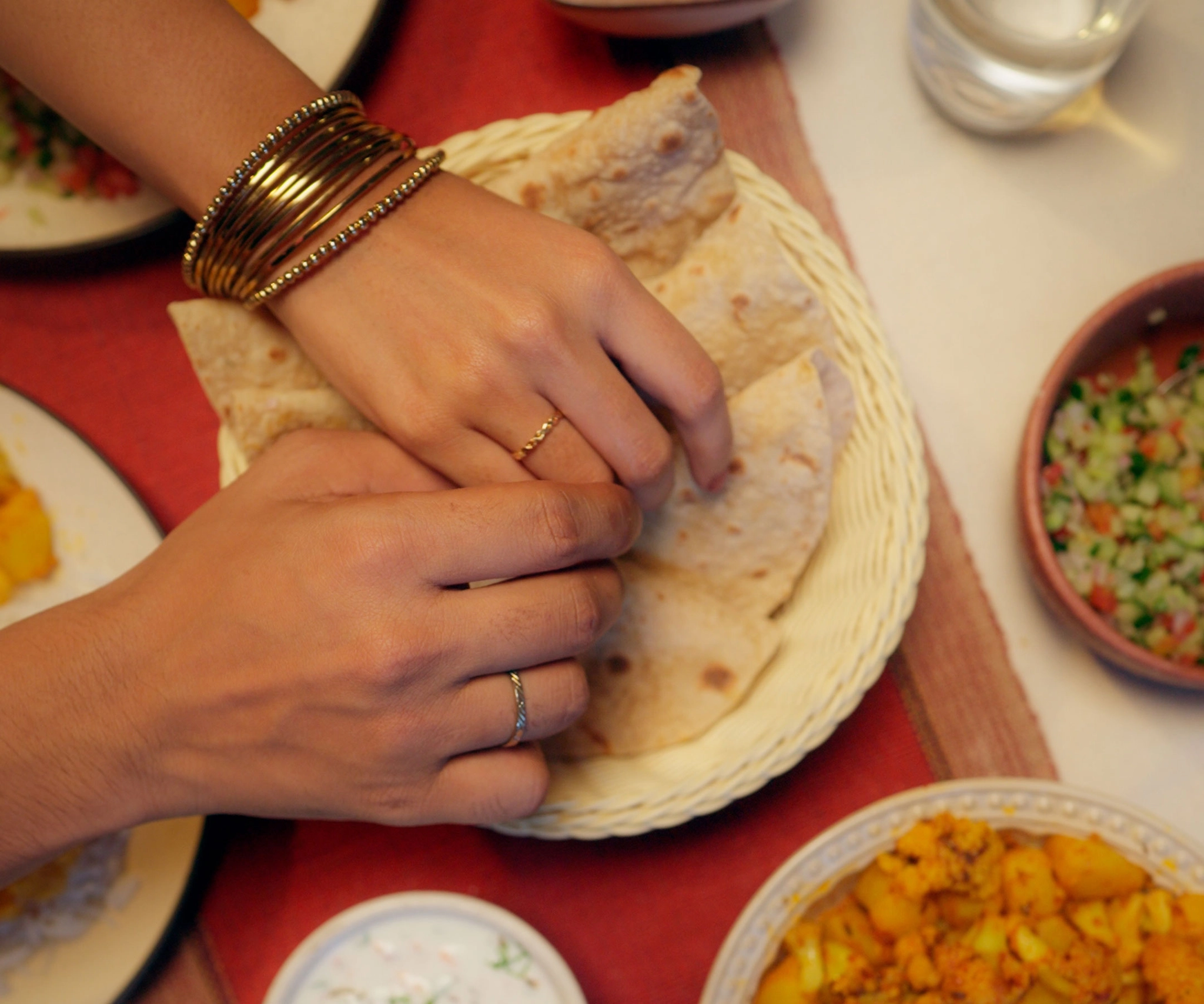 Flatlay image of a table spread, one male and female hand reaching out for the rotis, high quality visual from a visual ad campaign