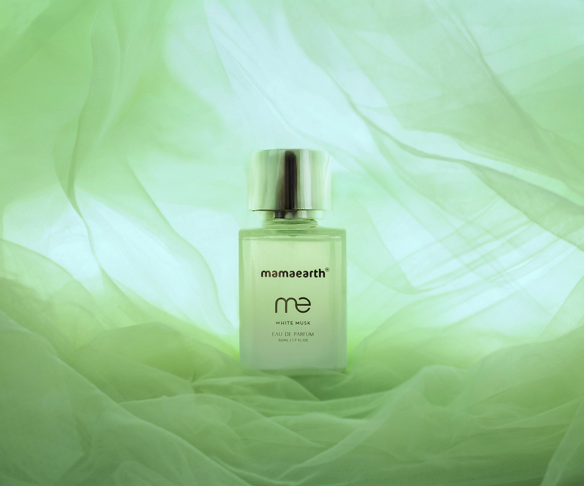 Mama earth's white musk perfume bottle kept on top of a green fabric, front angle wide shot of the setup, backlight shot of the perfume