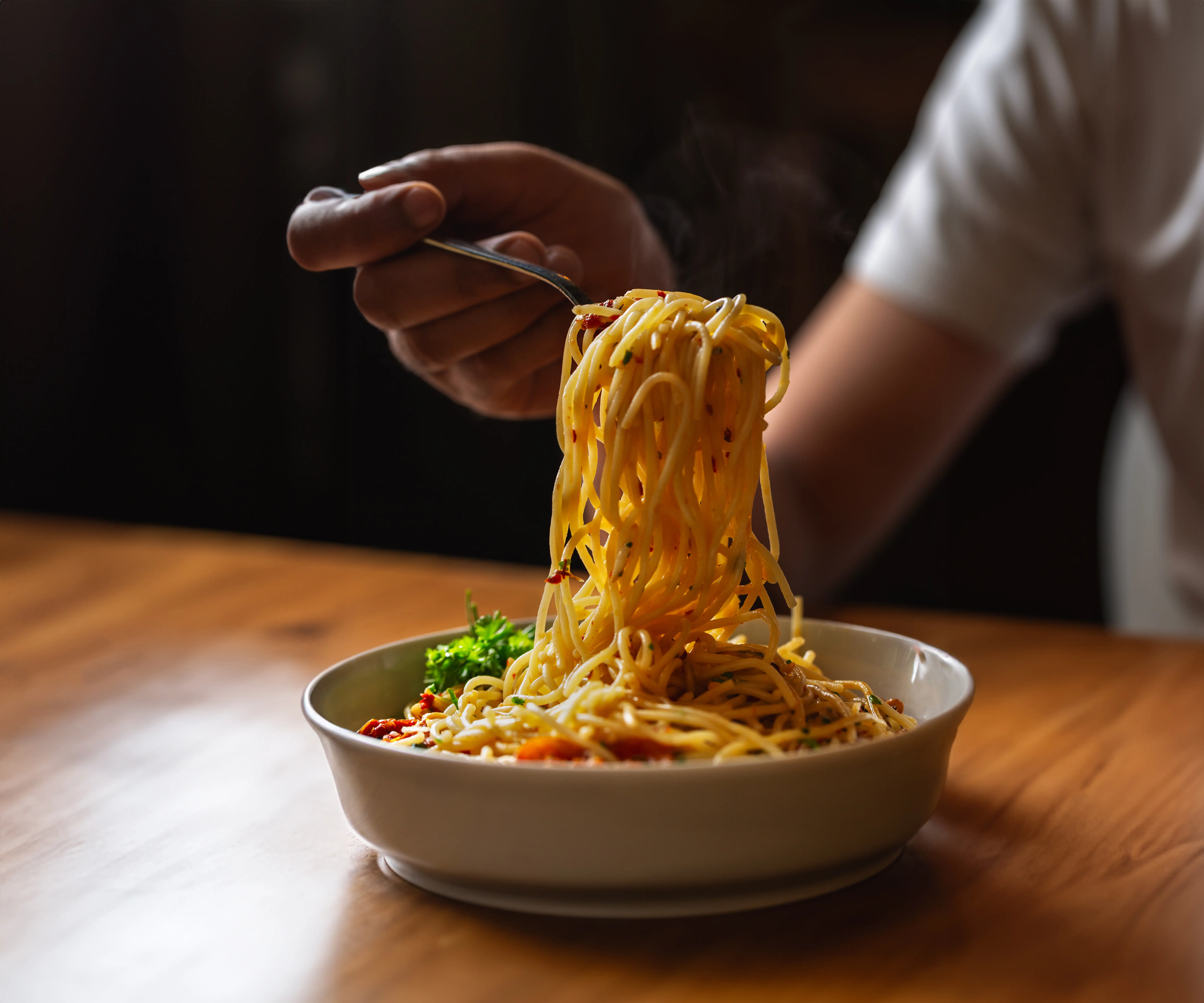 Photo of a band holding up a spoonful of spaghetti aglio olio in a moody background, high contrast food photography for a restaurant in bangalore