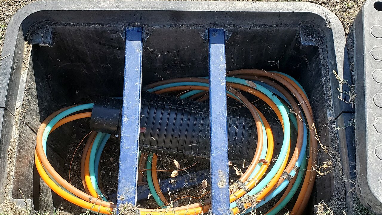 Orange and teal fibre optic cables coiled inside a black underground junction box with blue support bars