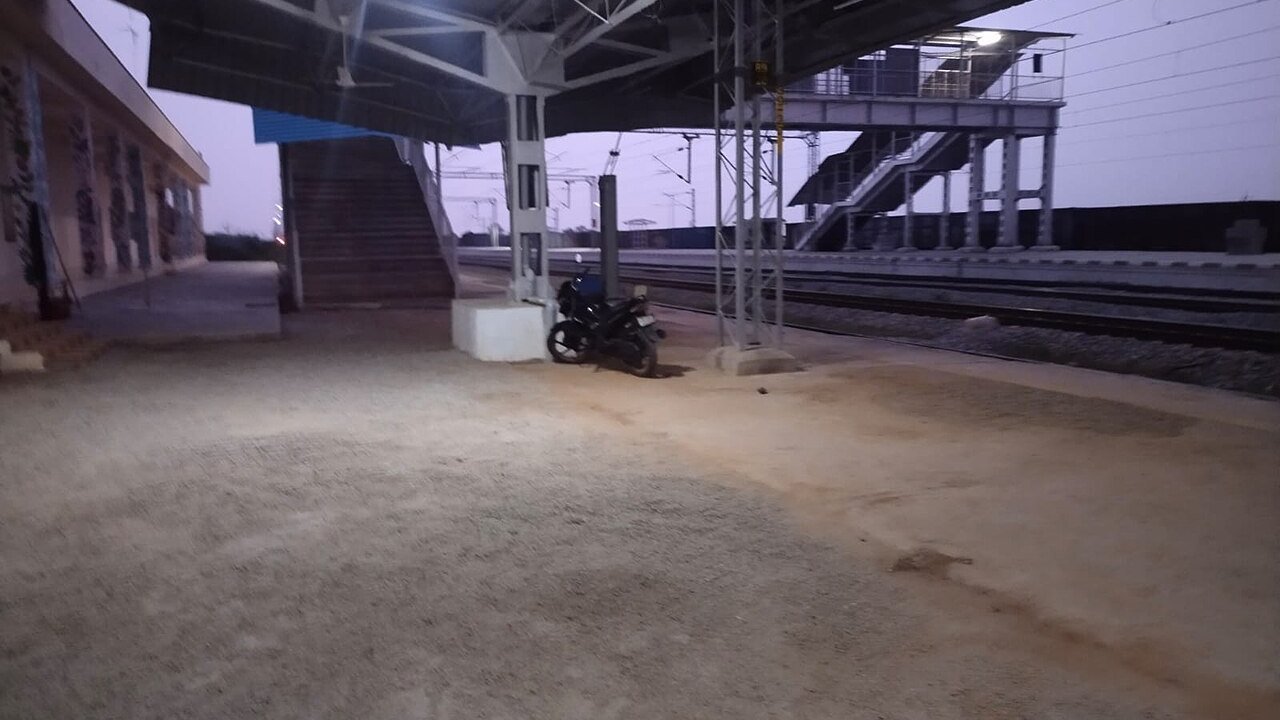 An unfinished railway platform with a footbridge, tracks and a parked motorcycle at dusk