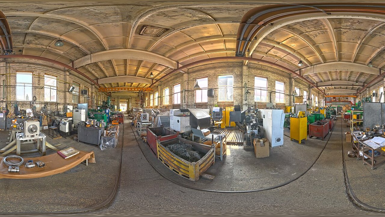 A large machine shop interior with lathes, cutting machines, yellow storage bins and metal scrap in an arched industrial hall.
