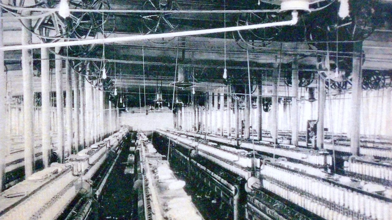 A cotton mill spinning room with long rows of machines, in an old photograph