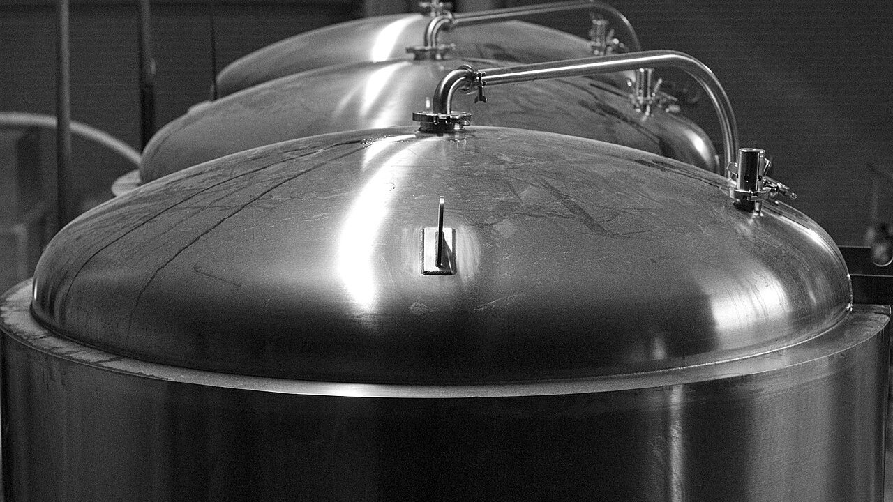 Polished stainless steel brewing tanks with domed tops and pipe fittings, shown in black and white.