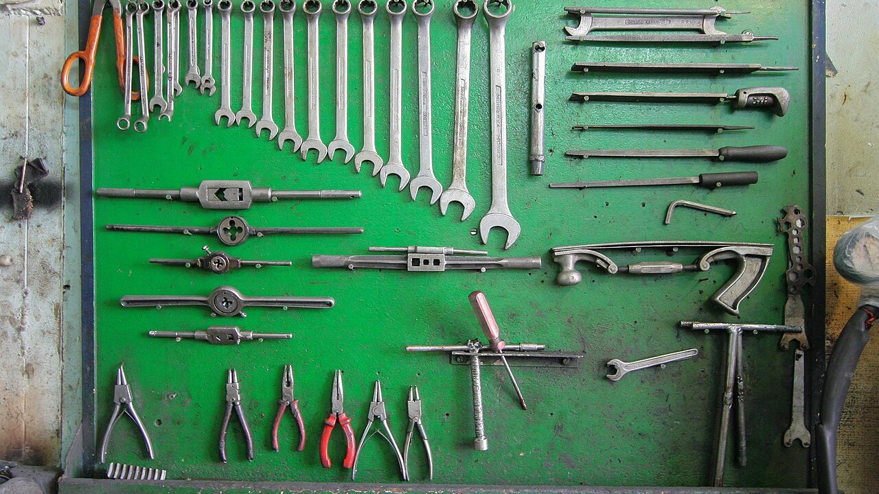 A green pegboard holding rows of steel hand tools including wrenches, tap wrenches, and pliers.