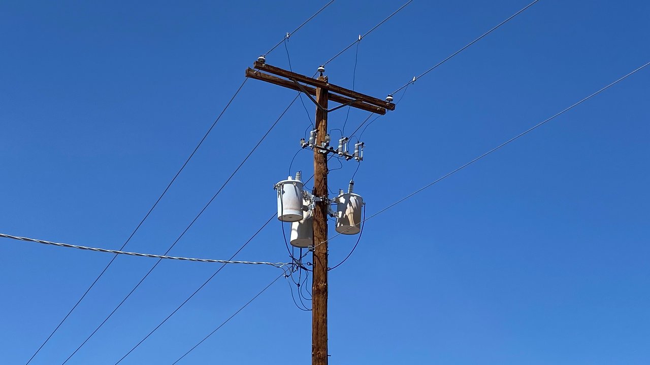 A wooden utility pole carrying distribution transformers and power lines against a clear blue sky