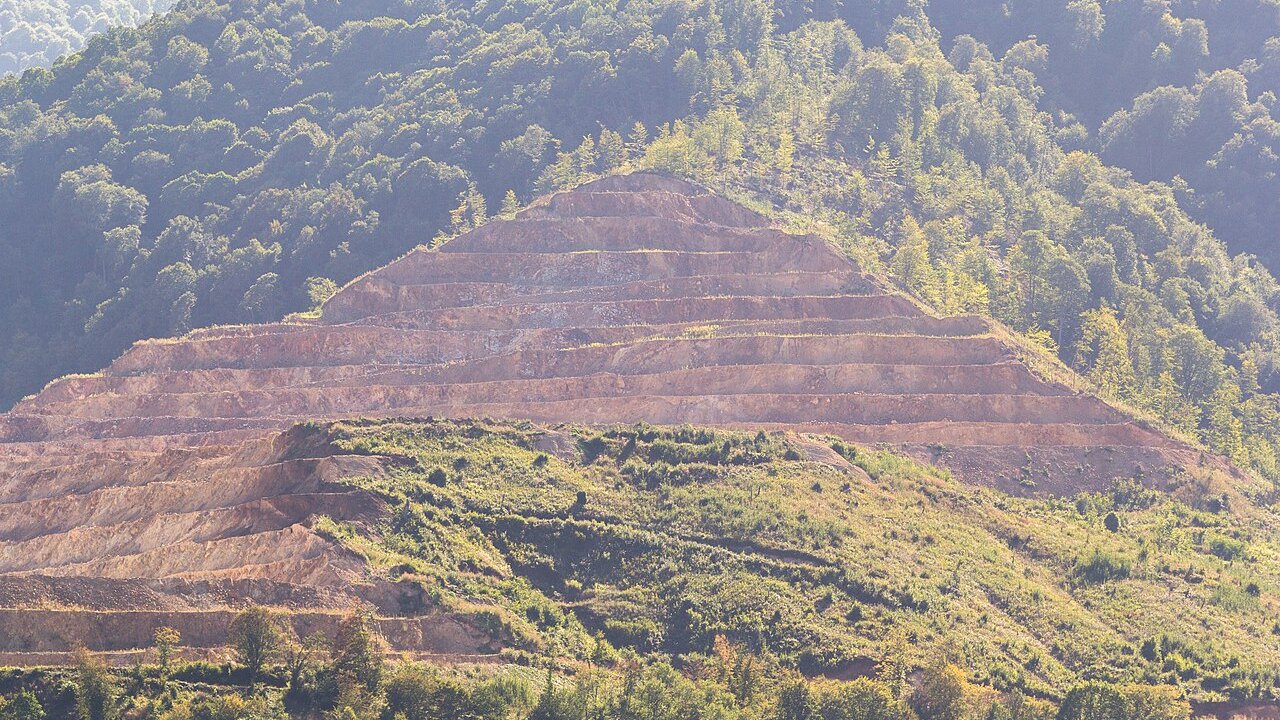 An open-pit mine with terraced benches cut into a forested hillside