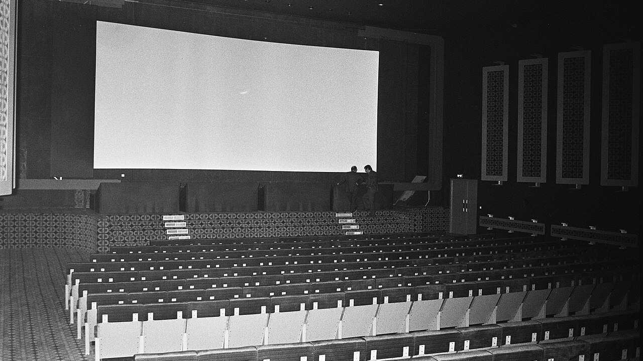 Black and white view of an empty cinema auditorium with rows of seats facing a large projection screen