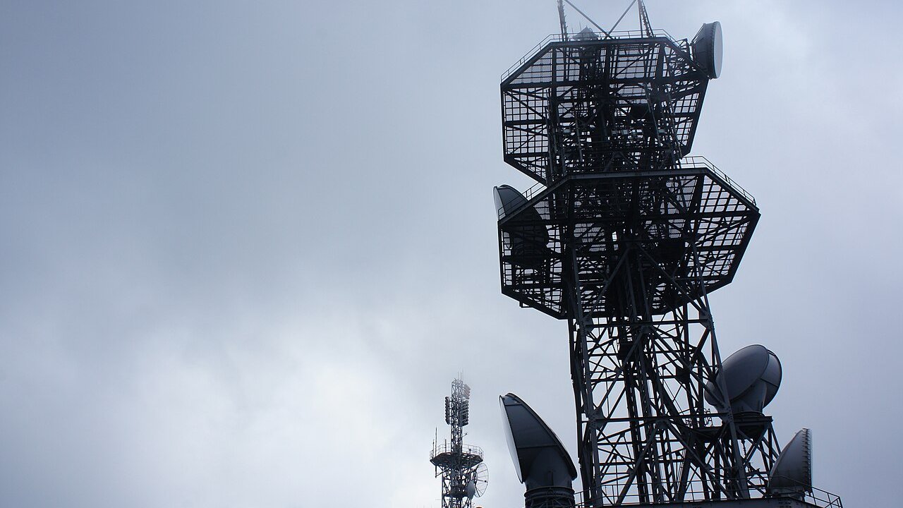 Lattice radio and telecommunications towers with dish antennas against a grey sky