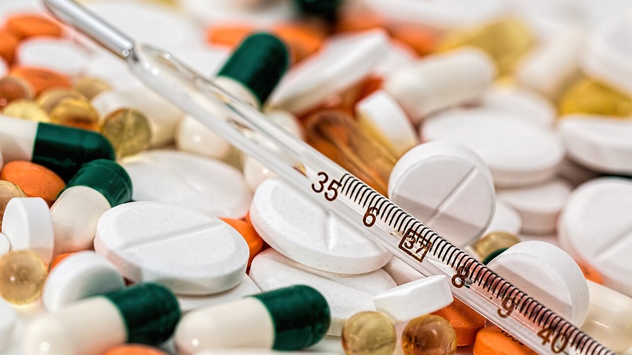 A pile of white and green-capped tablets and capsules with a glass thermometer lying across them.
