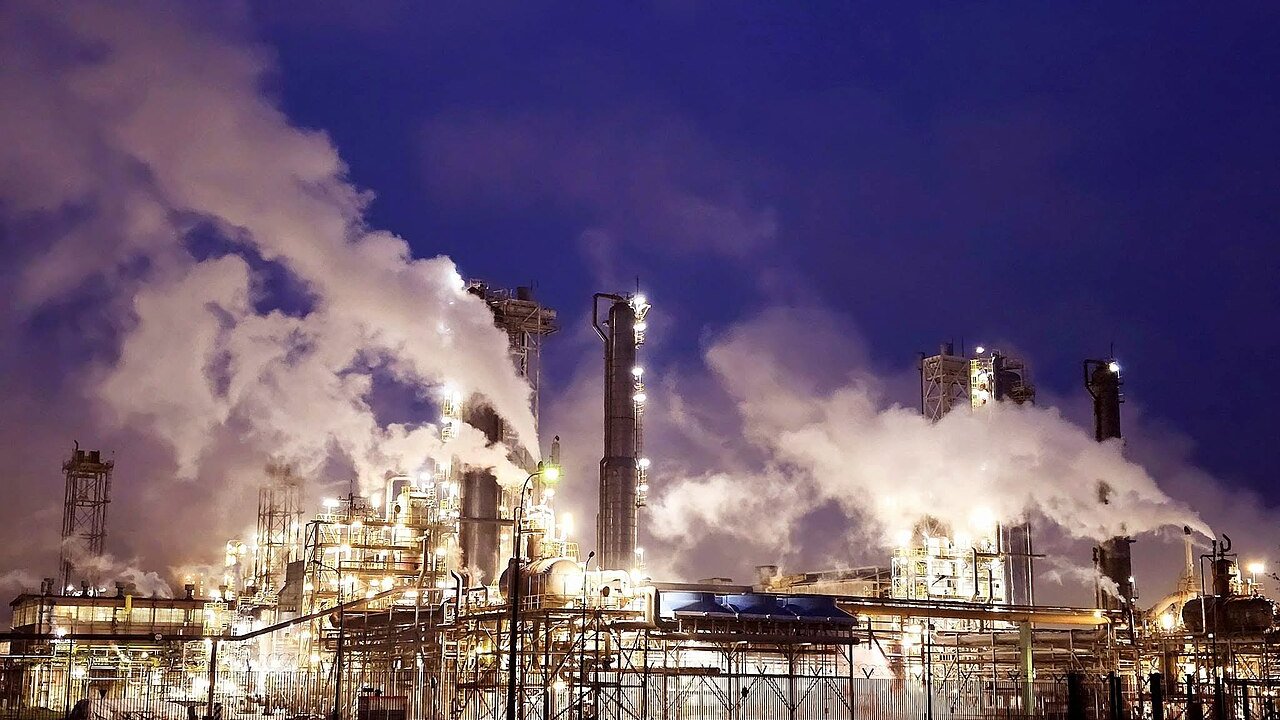 A chemical plant at night with lit pipework, towers and steam rising into the sky