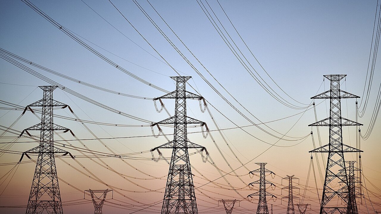 High-voltage transmission towers with power lines strung across them against a dusk sky.
