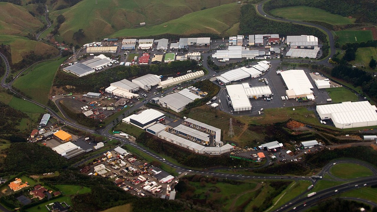 Aerial view of an industrial estate with large warehouse buildings, loading yards and roads set among green hills