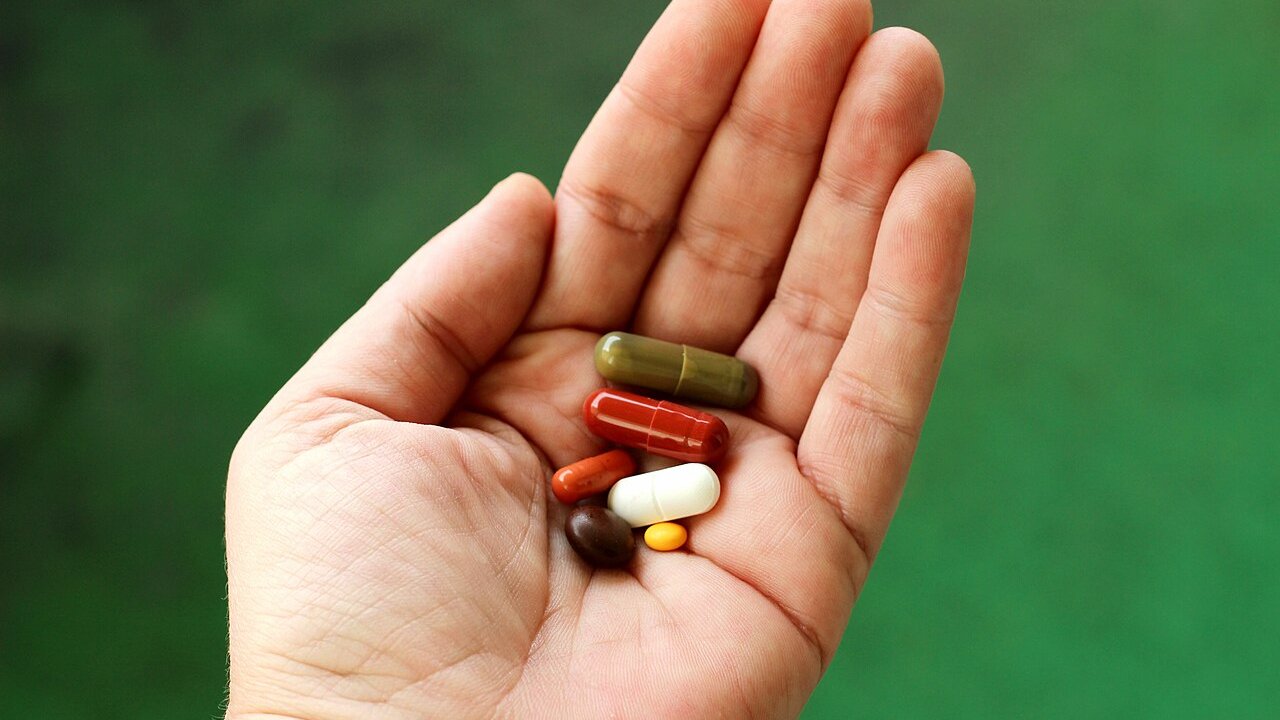 A hand holding a handful of assorted capsules and tablets against a green background
