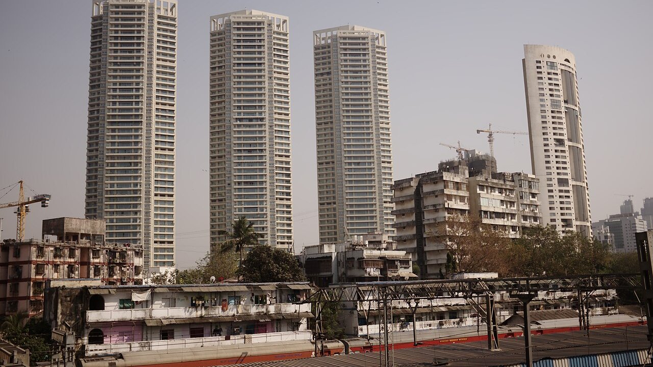 Several tall residential towers and older low-rise buildings above a railway line in a city, with construction cranes behind them.