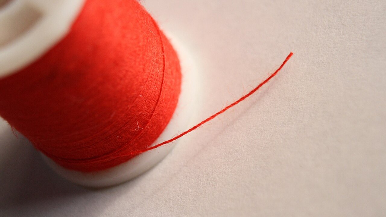 A spool of red thread with a length of thread unwinding across a light background.