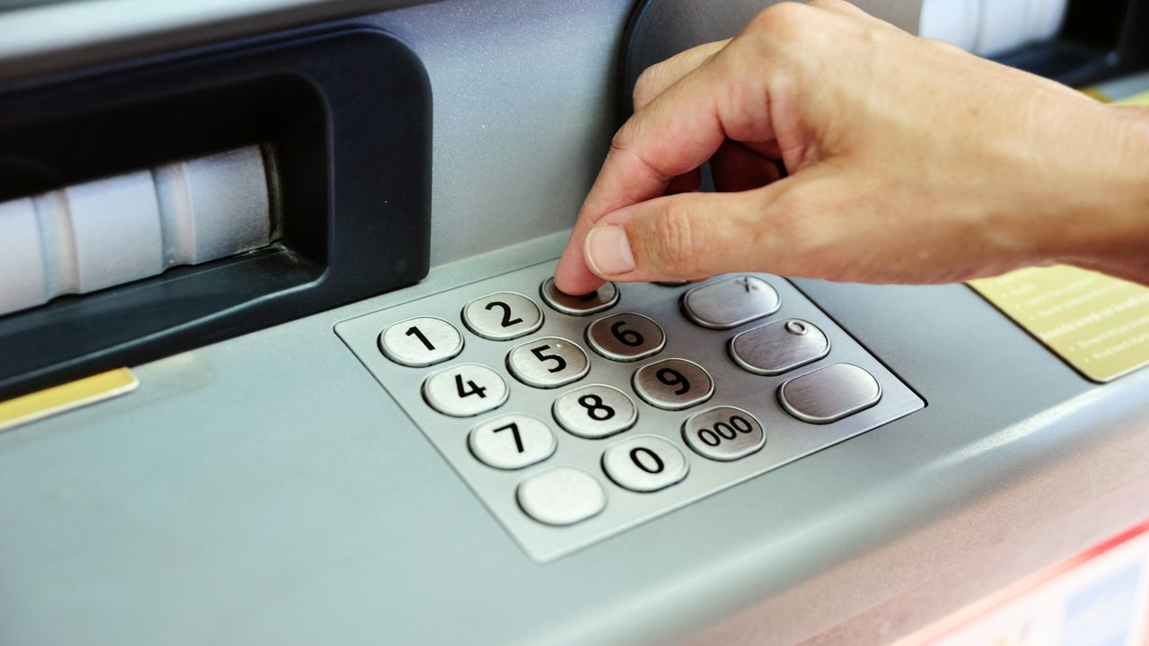 A hand entering a PIN on an ATM keypad.