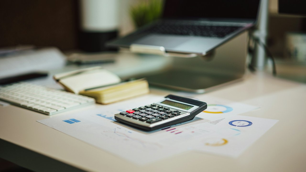 A calculator on a table next to a laptop.