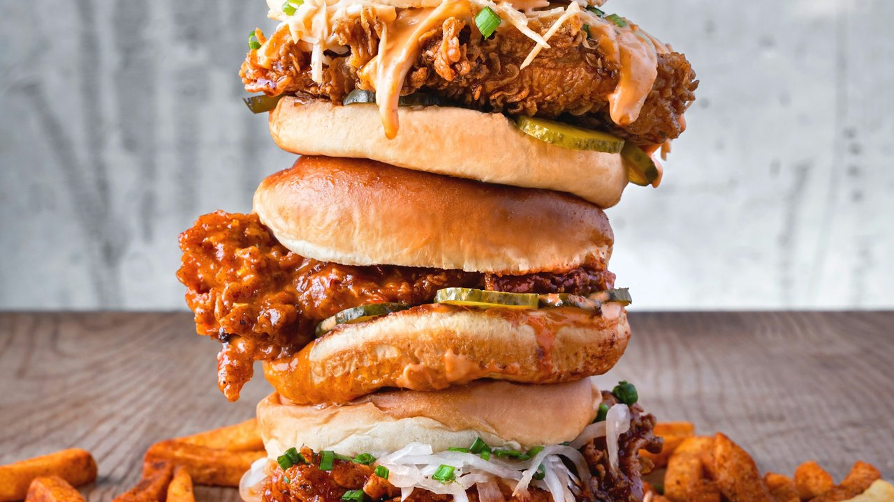 Stacked fried chicken burgers with fries on a wooden table.