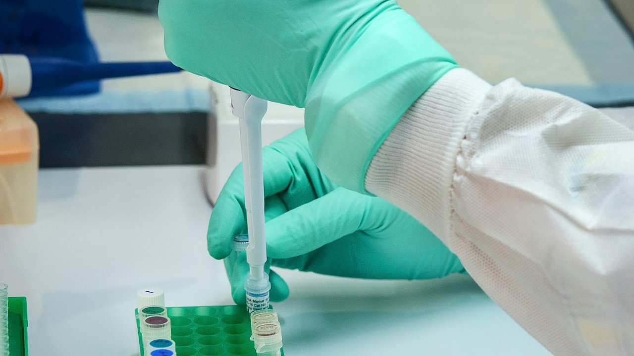 A gloved hand using a pipette over sample vials in a laboratory.