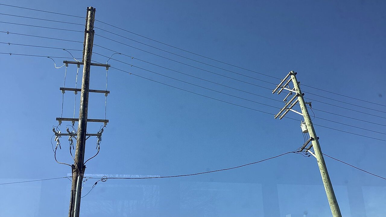 Two wooden-and-steel electricity poles carrying overhead power lines against a clear blue sky.