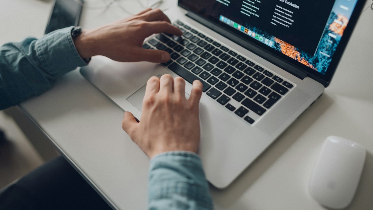 Hands typing on a laptop on a white desk.