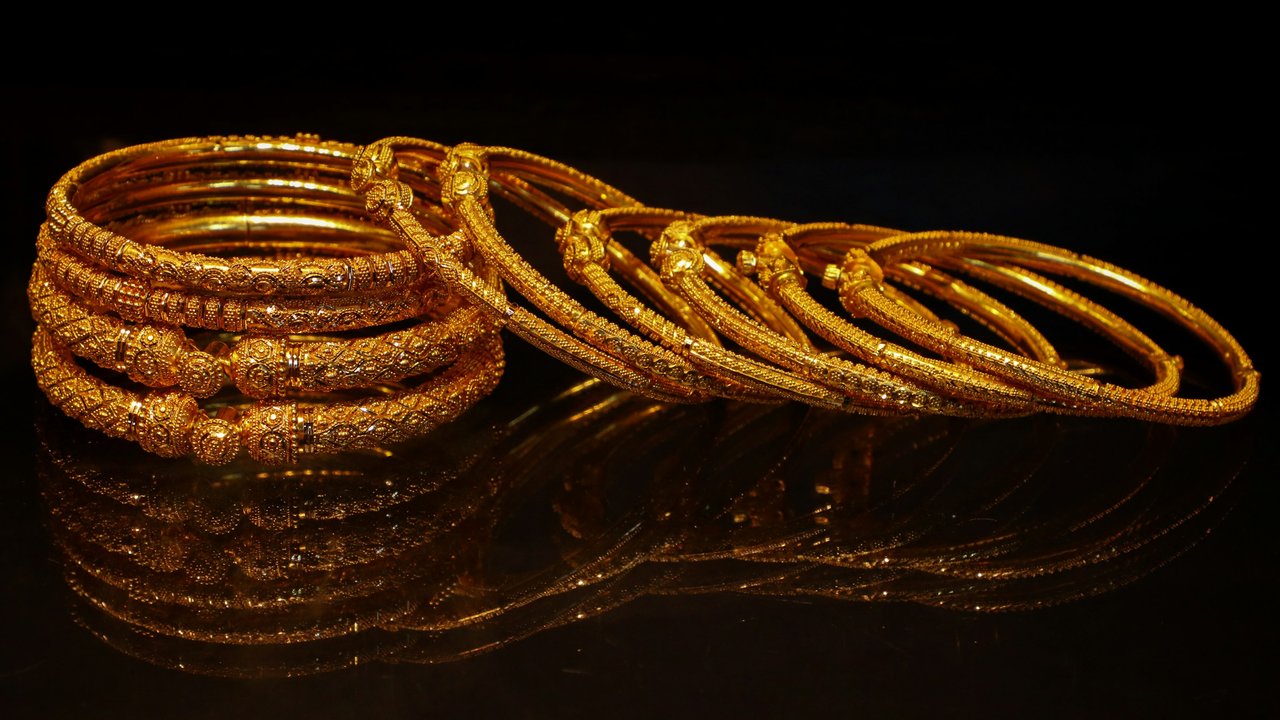 A set of ornate gold bangles on a reflective black surface.