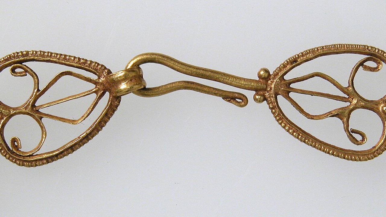 A gold filigree clasp with two oval openwork ends and a hook fastener on a plain background