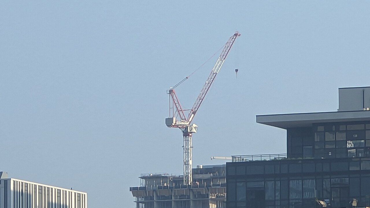 A white and red construction crane beside a half-built multi-storey building under a clear sky