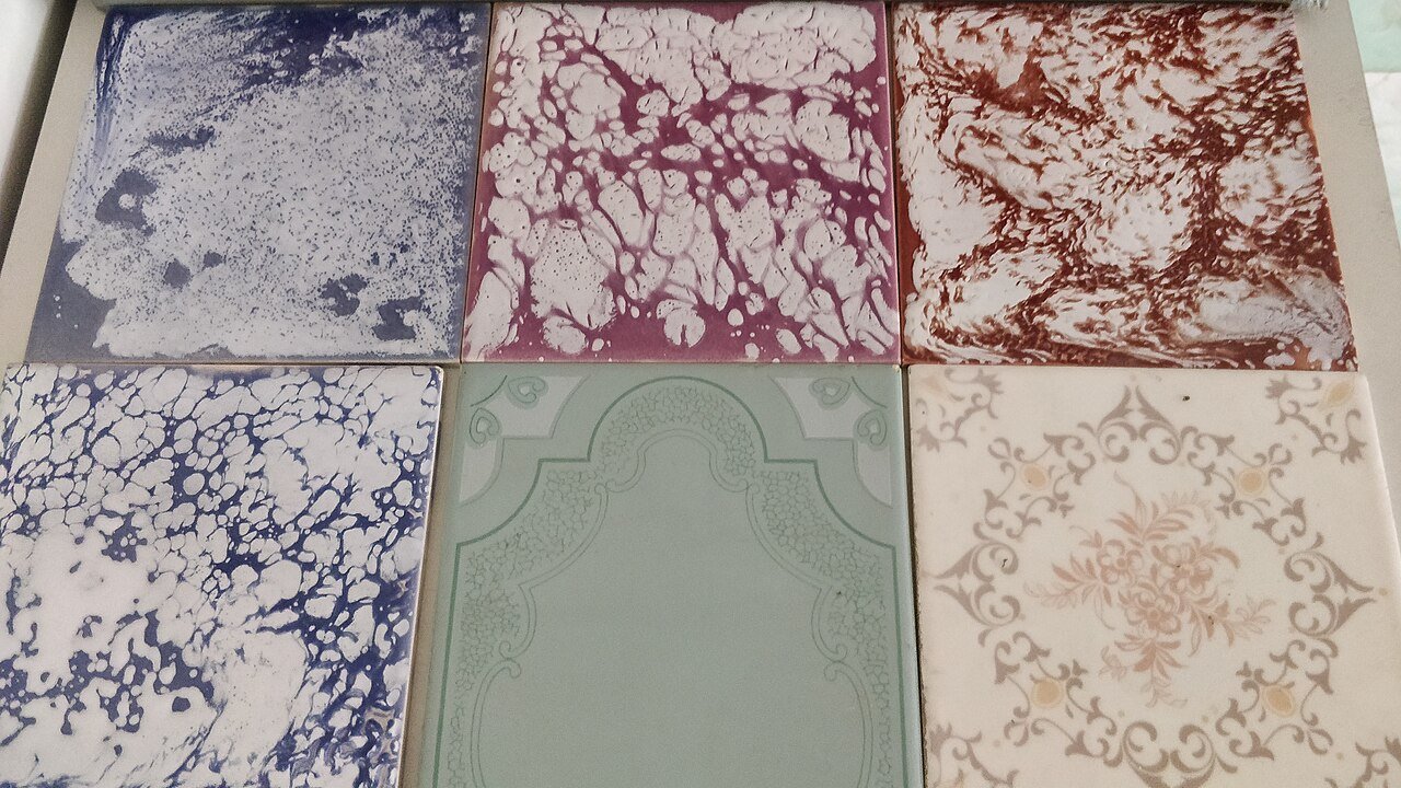 Six ceramic wall tiles in marbled blue, purple, red and white patterns, plus a pale green embossed tile and a beige floral-motif tile.