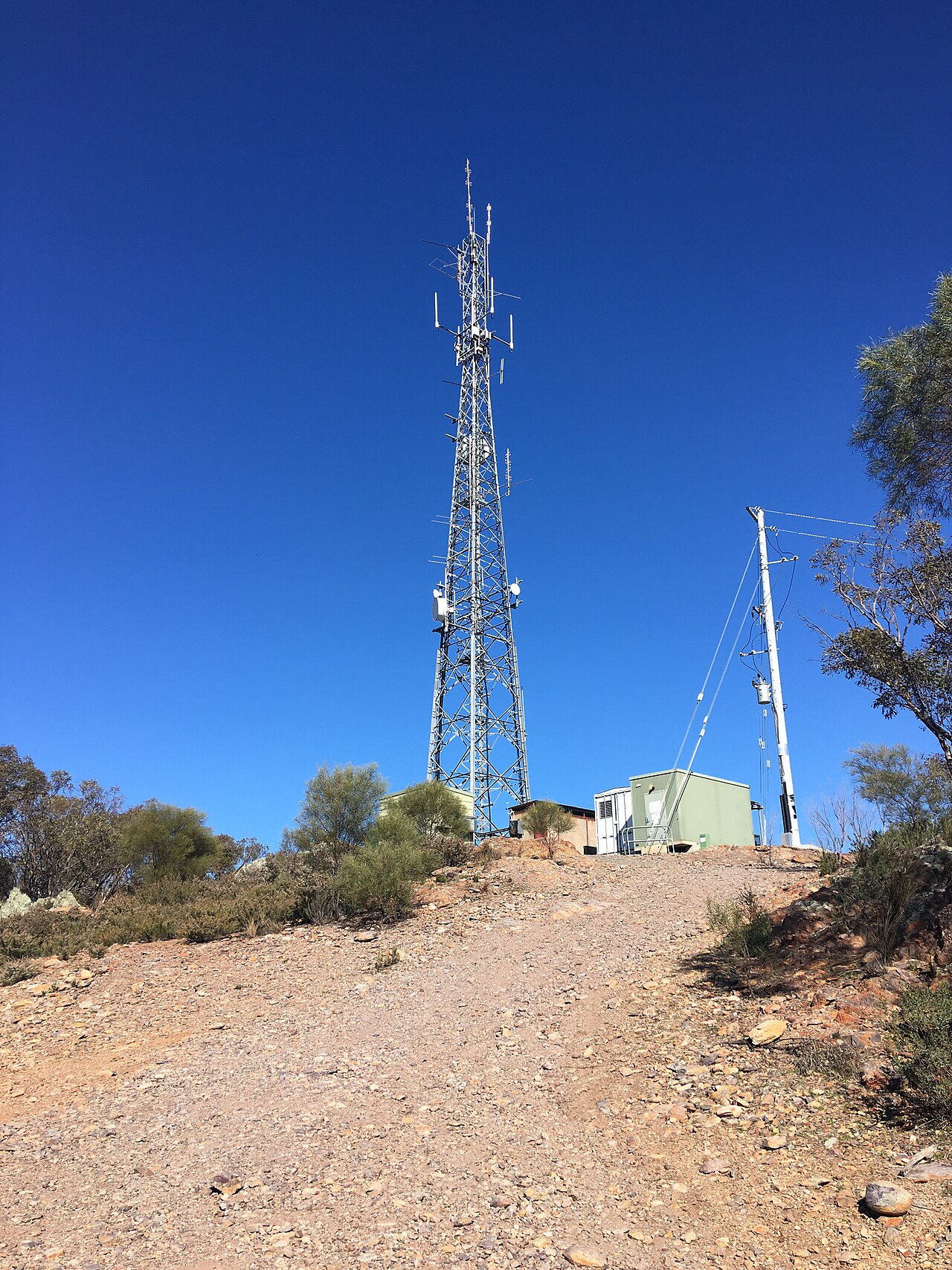 A telecommunications tower on a hilltop beside a small equipment hut