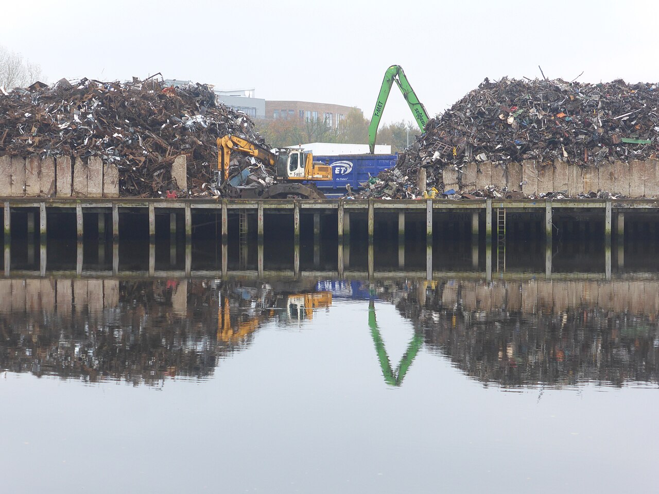 A scrap metal yard with piles of metal and a crane beside the water