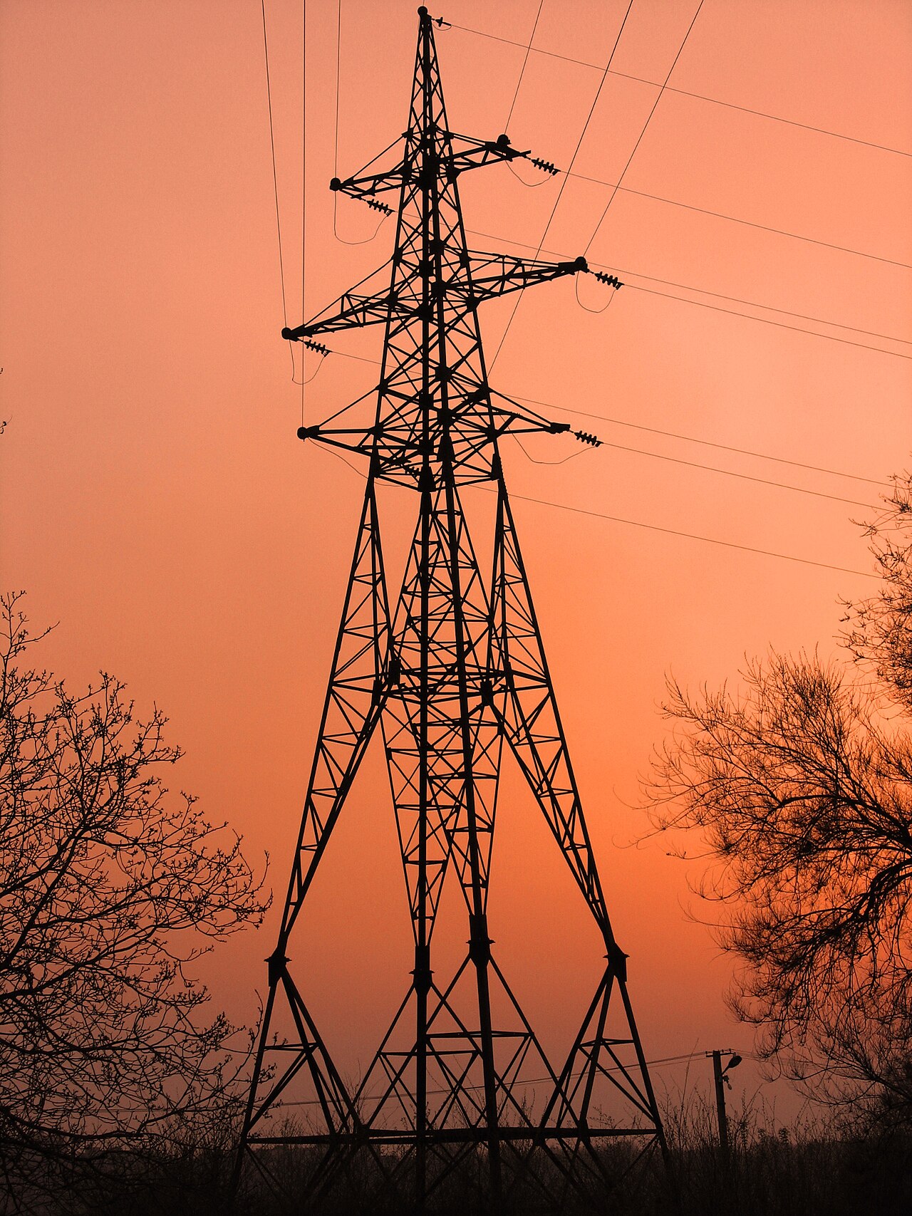 A steel transmission tower silhouetted against an orange sky