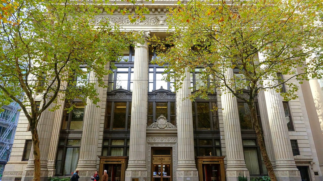 A stone bank building with tall columns and trees in front
