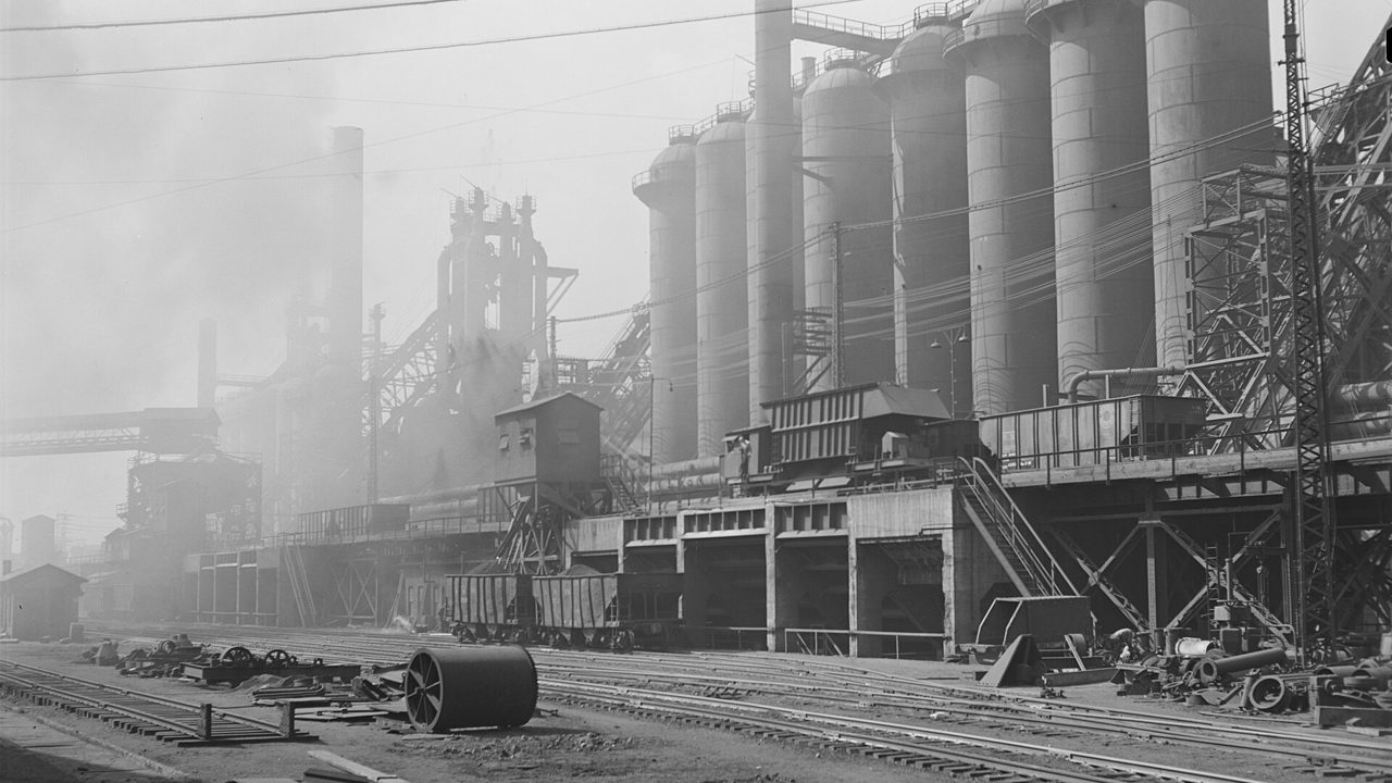 A steel mill with blast furnaces and storage towers, in an old black-and-white photograph