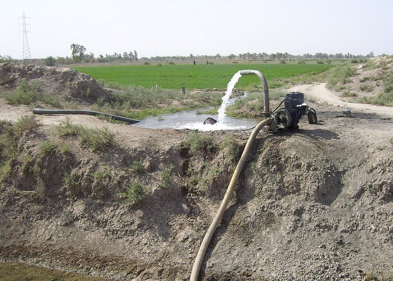 A pump sending water into an irrigation channel beside a green field