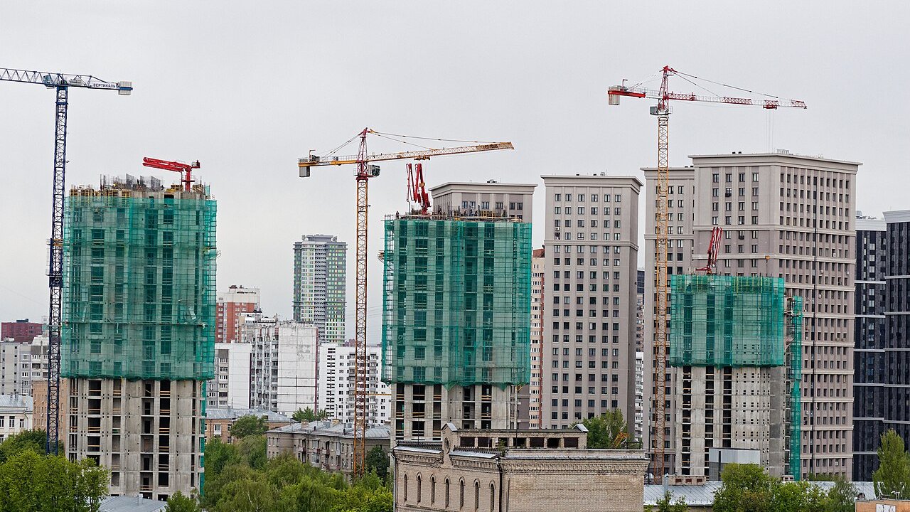 Several high-rise residential towers under construction, with cranes and green safety netting covering the concrete frames