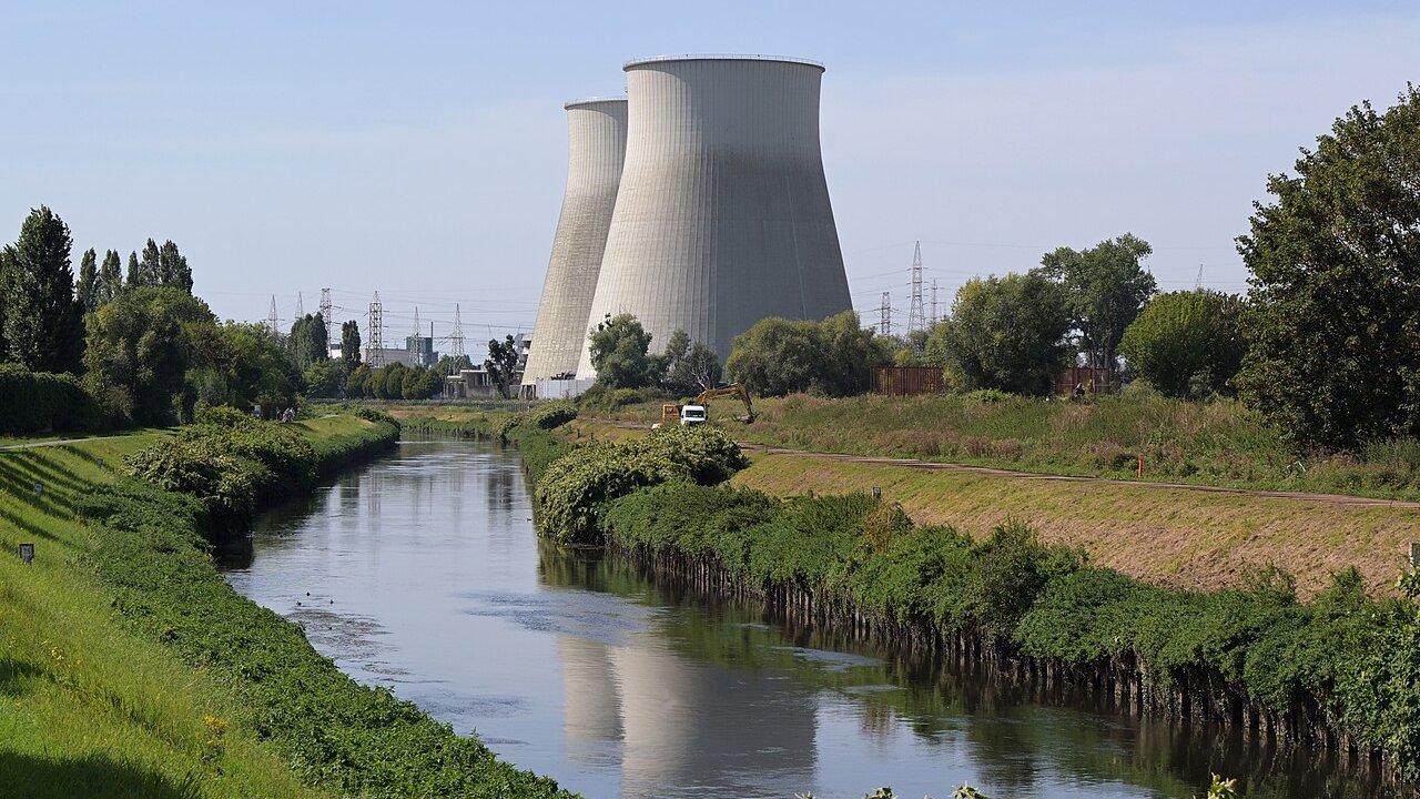 Two large concrete cooling towers of a power plant beside a canal with grass banks and power lines