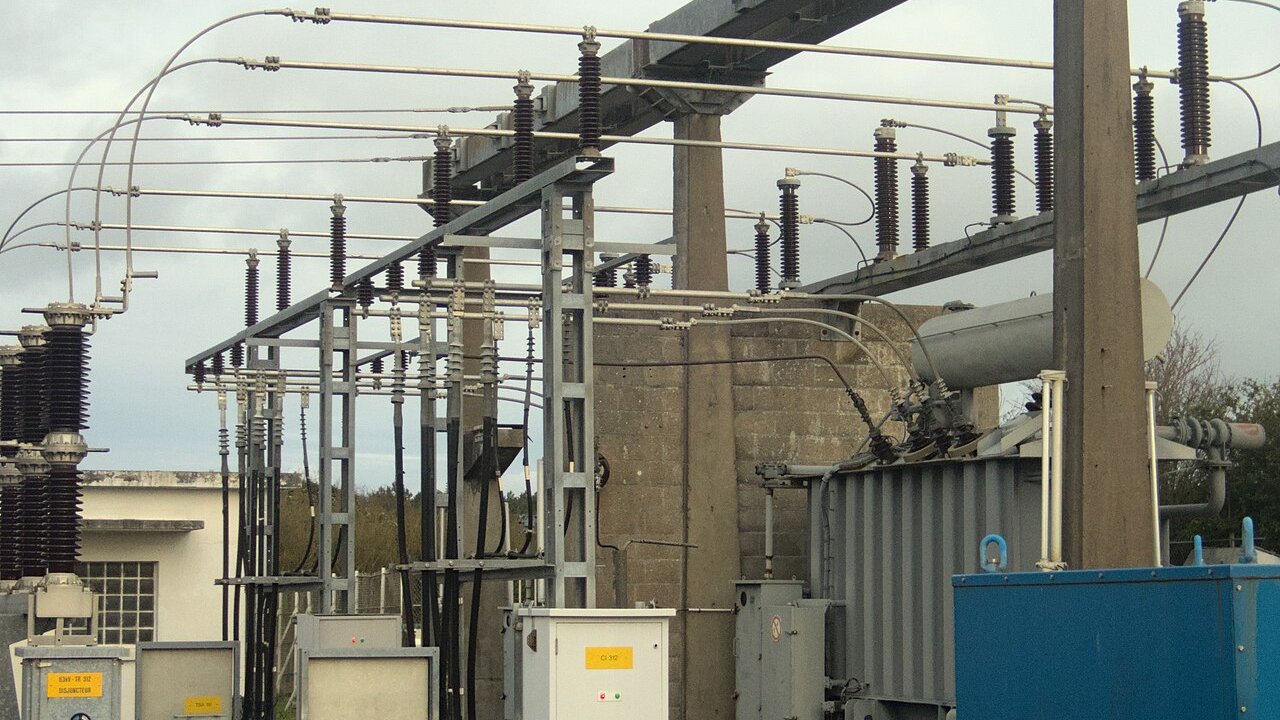 An outdoor high-voltage electrical substation with transformers, insulators and overhead busbars