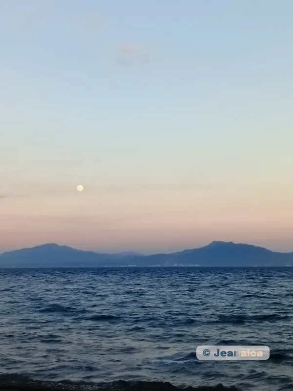 A picture of the sunset on the sea with mountains