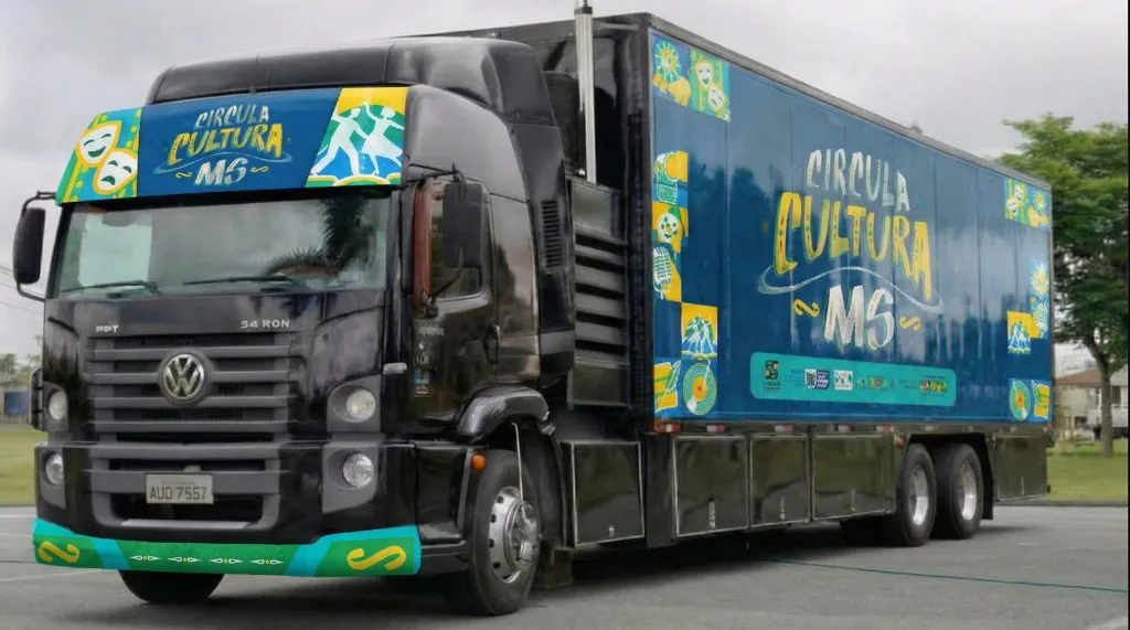 Foto em perspectiva da parte frontal e lateral esquerda da carreta palco preta do Circula Cultura MS. O cavalo mecânico exibe o adesivo do projeto no defletor de ar superior. A carroceria azul exibe a marca em grande destaque.